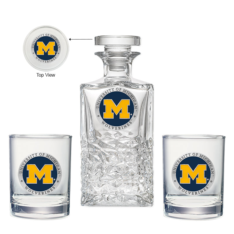 Glass decanter and two glasses with University of Michigan Wolverines logo on a white background