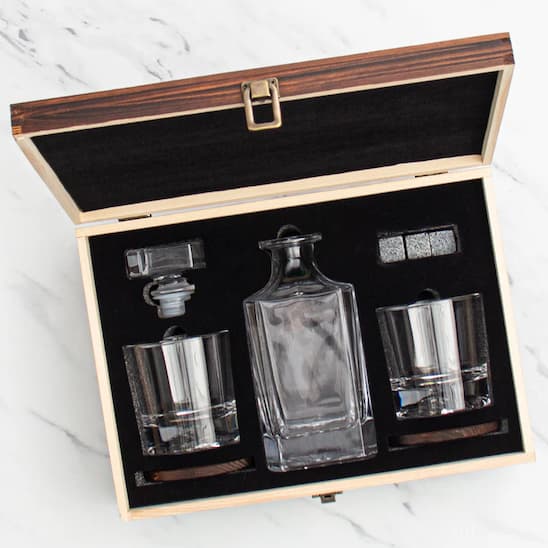 Glass decanter set with two glasses in a wooden box on a white marble surface