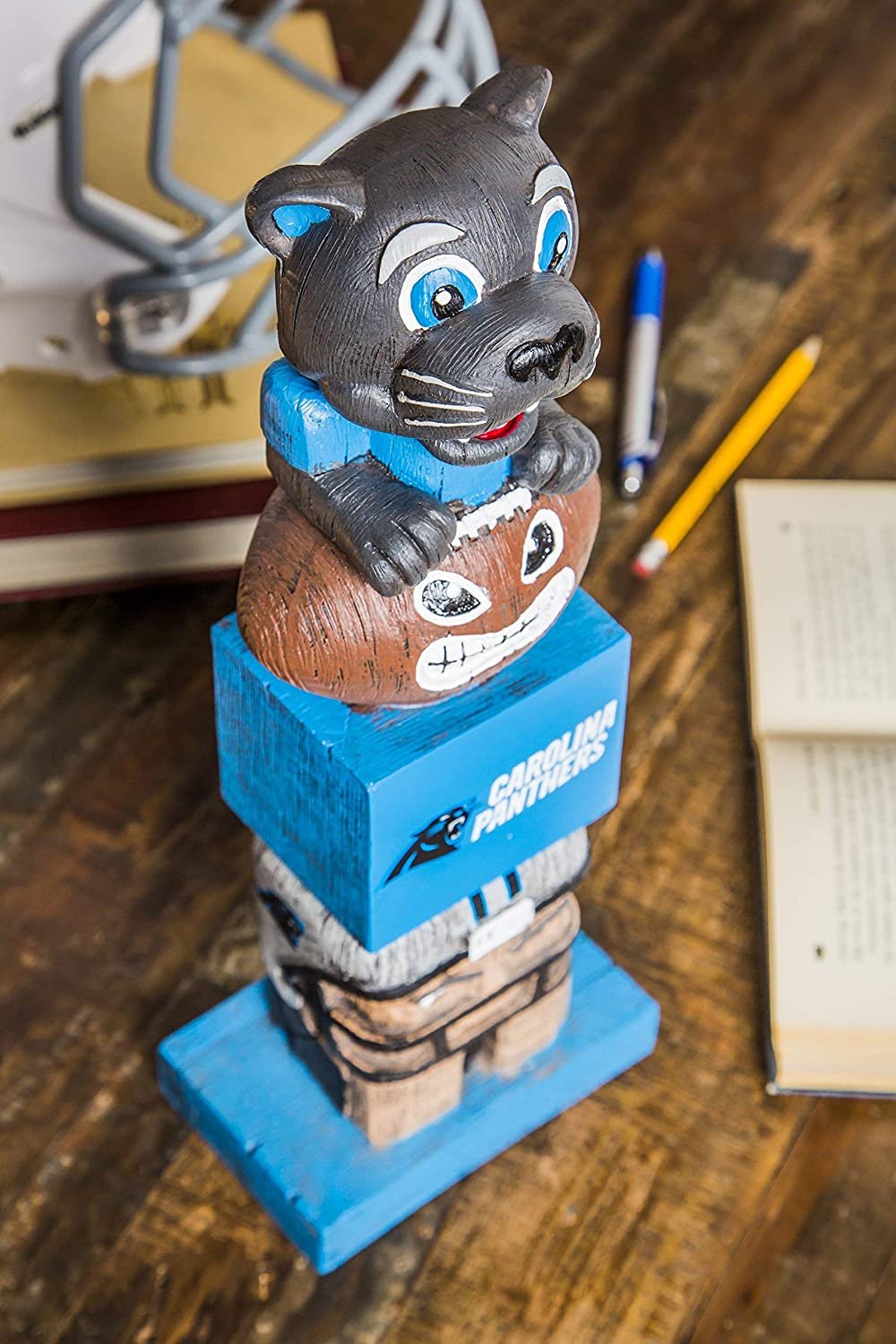 Wooden bobblehead figure of a panther on a blue base with a sports team logo, placed on a wooden surface with stationery items.